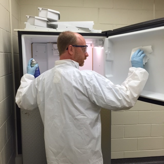 man cleaning freezer wearing safety glasses, lab coat, and gloves